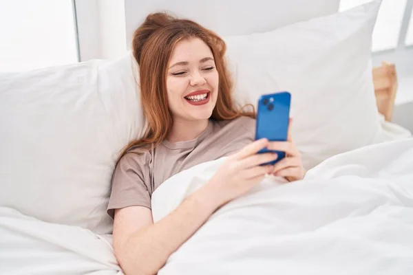 Νεαρή Κοκκινομάλλα Γυναίκα Που Χρησιμοποιεί Smartphone Ξαπλωμένη Στο Κρεβάτι Στο — Φωτογραφία Αρχείου