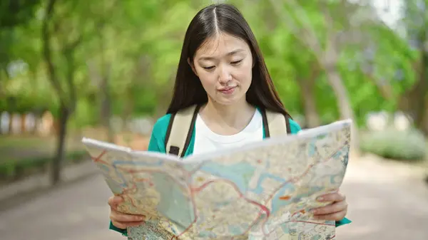 Young chinese woman tourist wearing backpack looking at city map at park