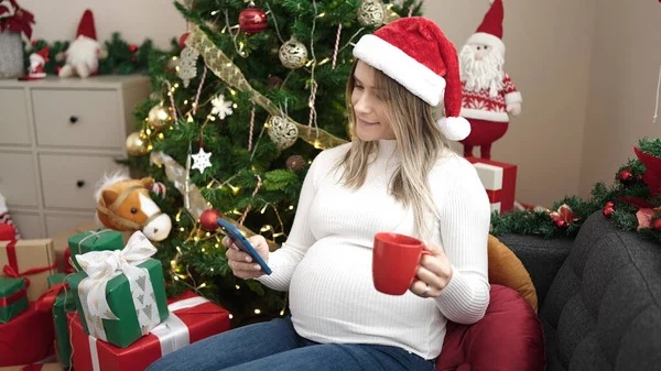 Mladá Těhotná Žena Pomocí Smartphone Pití Kávy Slaví Vánoce Doma — Stock fotografie