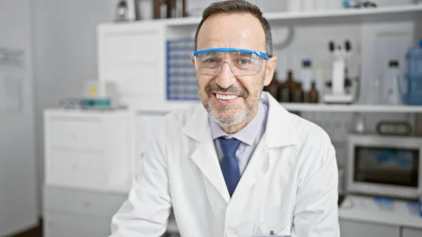 Confident middle age man, grey-haired, happy scientist wearing security glasses, studied research and science, loving his work in the medicine lab, sporting a smile.