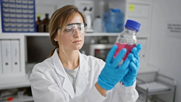 In the heart of medical science, young, beautiful blonde scientist engrossed in her groundbreaking experiment, expertly measuring liquid in a bottle at her lab workstation