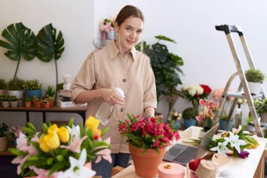 Genç beyaz kadın çiçekçi çiçekçide dağıtıcı sulama bitkisi kullanıyor.