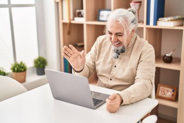 Middle age grey-haired man having video call sitting on table at home