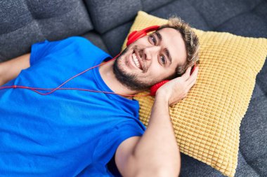 Young man listening to music lying on sofa at home