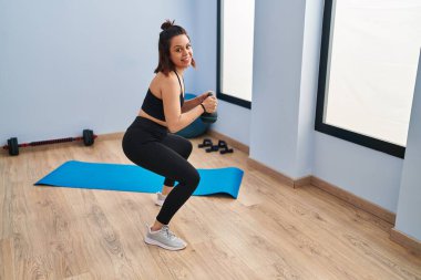 Genç, güzel İspanyol kadın gülümsüyor spor merkezinde kendine güvenen bacak egzersizi yapıyor.