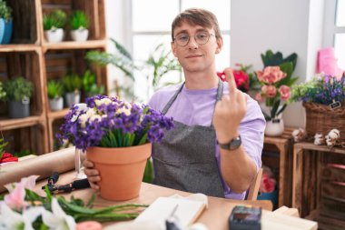 Caucasian blond man working at florist shop showing middle finger, impolite and rude fuck off expression 