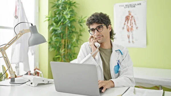 Young Hispanic Man Doctor Using Laptop Talking Telephone Clinic — Stock Photo, Image