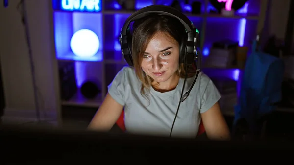 笑顔の若いブロンドストリーマーの女性 彼女のゲームルームで喜んでビデオゲームをプレイし 彼女の素晴らしいバーチャルアドベンチャーをライブストリーミング ゲーム テクノロジー そして魅力が暗闇の中で輝く — ストック写真