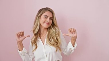 Genç ve kendinden emin, tişörtlü sarışın bir kadın gururlu bir poz veriyor, kendini parmağıyla işaret ediyor, mutluluk saçıyor. Pembe bir duvara karşı tek başına duruyor, aya bakıyor..