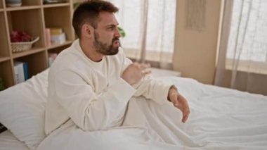 Genç İspanyol adam kaşınmak için kolunu tırmalıyor. Yatak odasında oturuyor.