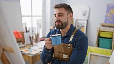 Sakallı, genç İspanyol erkek sanatçı, gözlerinde şüphe, sabah kahve fincanını emziriyor, derin düşüncelere dalmış, hareketli sanat stüdyosunda yeni çizilmiş bir tuvale bakıyor..