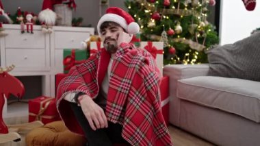 Genç İspanyol adam Noel ağacının yanında oturmuş üzgün üzgün bakıyor.