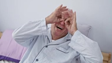 Tuhaf yatak odası maskaralıkları, yatakta oturan yaşlı adam, sallanan pijamalar, 'tamam' işareti parmaklarından bakan, şakacı ifadeyle dilini dışarı çıkaran