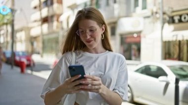 Young blonde woman smiling confident making selfie by the smartphone at street