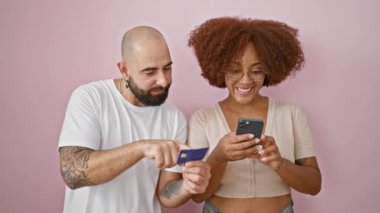 Akıllı telefon ve kredi kartıyla izole edilmiş pembe arka planda kutlama yapan güzel çift.