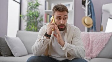 Evdeki oturma odasındaki kanepede oturmuş akıllı telefonuyla tartışan sinirli, genç bir İspanyol.