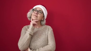 Gri saçlı, gülümseyen orta yaşlı bir kadın izole edilmiş kırmızı arka planda parmaklarıyla fikir jesti yapıyor.