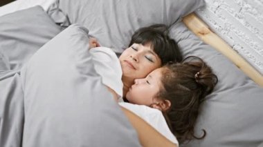 Sıcak odalarında birlikte uzanan bir anne ve kız, aile evlerinin yumuşak yatağında uykuya dalmadan önce sevgi dolu bir kucaklaşmayı paylaşıyorlar..