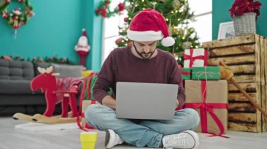 Genç İspanyol adam dizüstü bilgisayar kullanıyor evde Noel 'i kutlamak için kahve içiyor.