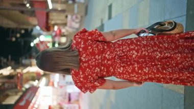 Osaka 'da enerjik bir gece, esmer İspanyol kadın, kendine güveni tam, Shinsekai caddesinde neşeli bir gülümseme sergiliyor, gözlüklerine yansıyan neşeli şehir ışıkları