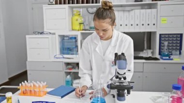 Bilimin kalbinde, genç, güzel İspanyol bilim kadını, işine dalmış, mikroskopla dikkatlice analiz ediyor ve laboratuarında notlar alıyor..
