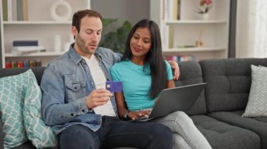Laptop ve kredi kartıyla alışveriş yapan güzel bir çift evdeki koltukta oturuyor.