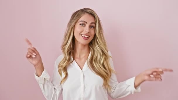 シャツを着た若い金髪の女性は 孤立したピンクの背景の上に大きな笑顔を身に着けながら 明るくさまざまな方向を指しています 完璧な広告コピースペース 驚異的な広告の準備ができています — ストック動画