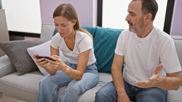 在家里 父亲和女儿就智能手机的使用进行了激烈的争论 他们不幸地坐在客厅的沙发上 在随意而紧张的谈话中表达了他们的不同意见 — 图库视频影像