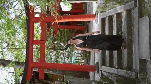 陽気で美しく メガネをかけたヒスパニックな女性が自信を持ってカメラに向かって歩き 背景にある歴史ある京都の寺院を照らす輝く笑顔 日本での楽しい旅行 — ストック動画