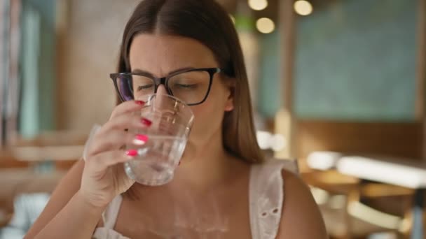 美丽的年轻女子 戴着眼镜 在食堂里喝着一杯水 — 图库视频影像