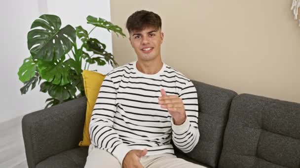 Розслаблений Молодий Іспаномовний Чоловік Виключаючи Впевненість Посміхаючись Зручно Сидячи Дивані — стокове відео
