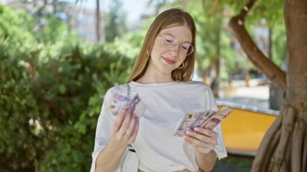 若い金髪の女性は自信を持って笑って公園でスウェーデンのクローネ紙幣を数える — ストック動画