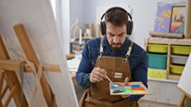 Yakışıklı İspanyol sanatçı, müzik eşliğinde dans eden genç adam, sanatını icra ederken kulaklıkla dinleyen, canlı bir üniversite sanat stüdyosunda tuvale resim çizen.