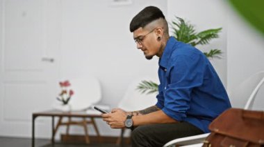 Stresli genç adam bekleme odasında oturmuş, ciddi ciddi akıllı telefonuyla mesaj atıyor.