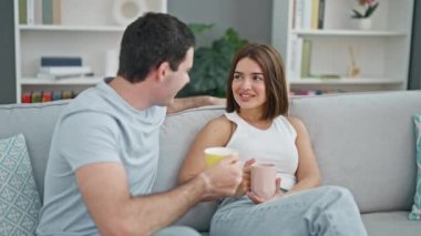 Kanepede birlikte oturan güzel bir çift evde gülümseyen bir kahve içiyorlar.