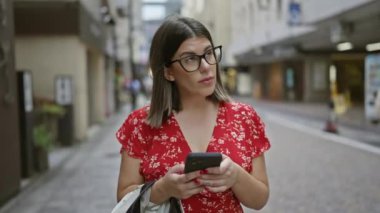 Tokyo 'da gözlüklü güzel İspanyol kadın. Şehir sokaklarında akıllı telefon aracılığıyla dijital bağlantı.
