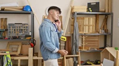 Genç, yakışıklı İspanyol marangoz akıllı telefonuyla konuşuyor. Marangozluk atölyesinde profesyonel bir çizim yapıyor.