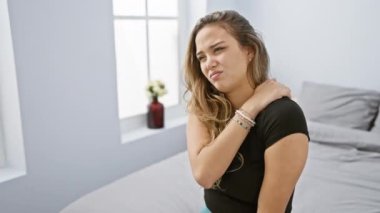 Güzel, genç İspanyol bir kadın, pijamalı, boyun ağrısı çekiyor, yatakta dinleniyor, ev içinde yaşam tarzını yansıtıyor yatak odasının iç kısımlarında rahatsızlığını yansıtıyor..