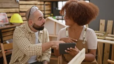 Marangozluk atölyesinde iş konuşan iki profesyonel marangoz, kereste ve mobilya inşaatı arasında dokunmatik alanda uzmanca geziniyorlar..