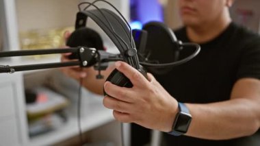 Ciddi genç Latin bir adam, akustik bir müzisyen, şarkısını yürekten söylüyor, müzik stüdyosundaki melodiye tamamen dalmış, kulaklık takıyor.