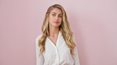 Sabırsız sarışın kadın, buluşmaya geç kalıyor, pembe arka planda kameraya bakarken izlemeyi işaret ediyor.