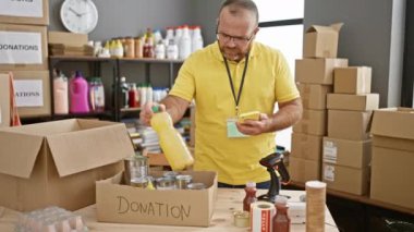 Sakallı, orta yaşlı, yakışıklı, beyaz adam kendini hayır kurumuna adamış bir gönüllü. Akıllı telefonunu kullanarak ürünleri kontrol ediyor. Topluma yardım eli uzatıyor..
