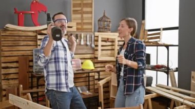 İki neşeli marangoz, bir erkek ve bir kadın, canlı mobilyalarında dans ederek ve müzikle sondaj yaparak ev içi marangozluk işyerlerinde