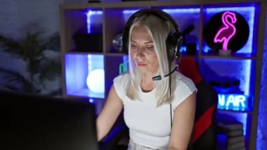 Sersemlemiş genç bir kadın, kulaklıklı şüpheci sarışın bir oyuncu karanlık bir oyun odasında bilgisayara bakarken şaşı gözlerle ve alaycı bir şekilde açık ağızla tepki veriyor..