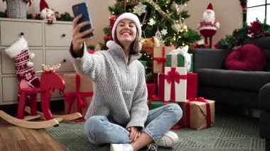 Genç ve güzel İspanyol bir kadın evdeki yılbaşı ağacının yanında oturmuş video görüşmesi yapıyor.