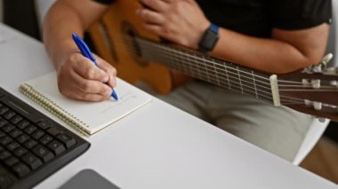 Tutkulu genç Latin bir adam, sanatının kalbinde bir müzisyen, klasik bir gitarı sıcacık bir müzik stüdyosunda tutarken bir melodi besteliyor.