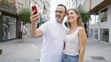 Kendine güveni tam bir baba-kız güzel bir anı paylaşıyorlar, neşeli bir şekilde cep telefonlarında serin bir selfie çekiyorlar hareketli bir şehir caddesinde duruyorlar..