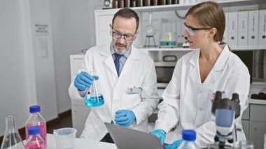 İki coşkulu bilimadamı laboratuarda birlikte çalışıyorlar, sohbet ediyorlar ve bir yandan da kapalı alandaki bilim araştırmalarında örnek analiz için bir test tüpü tutuyorlar..