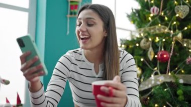 Genç ve güzel İspanyol kadın akıllı telefon kullanıyor. Evde Noel 'i kutlamak için kahve içiyor.
