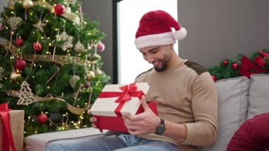 Genç Arap adam yılbaşı şapkası takıyor, hediyesini açıyor ve eve üzgün bakıyor.